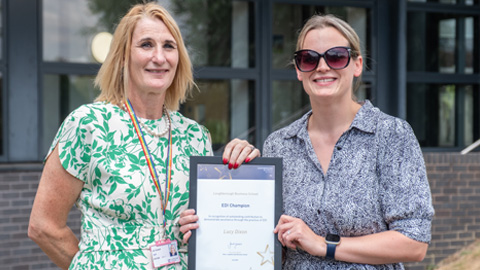 Two people standing side by side; one holds a framed award